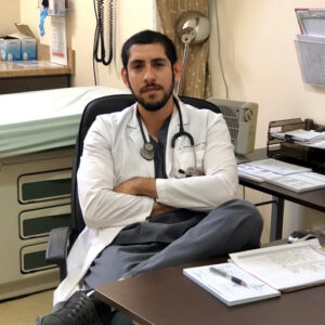 ethnic doctor wearing white medical coat sitting at desk