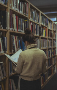 female calgary christian counsellor in beige sweater researching by shelf in library