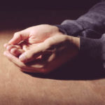 Man's open hands meditating or praying at a wooden table
