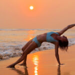 Woman in blue bikini performing yoga poseon beach during sunset