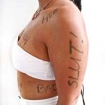 Woman in white crop top with words of shame that abuse writes on our hearts written on her body.